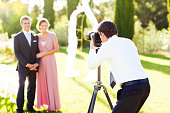 Man Photographing Groomsman And Bridesmaid At Garden Wedding