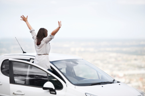 Young woman in her car overlooking a splendid view with her arms outstretched