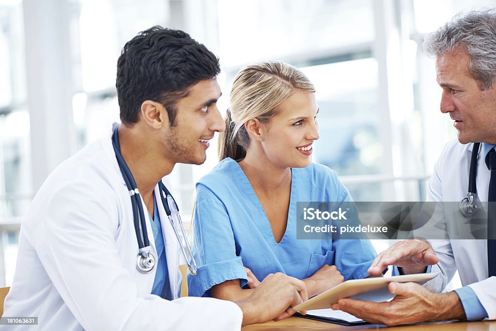 Confirming the diagnosis A group of doctors looking together at something on a digital tablet Adult Stock Photo