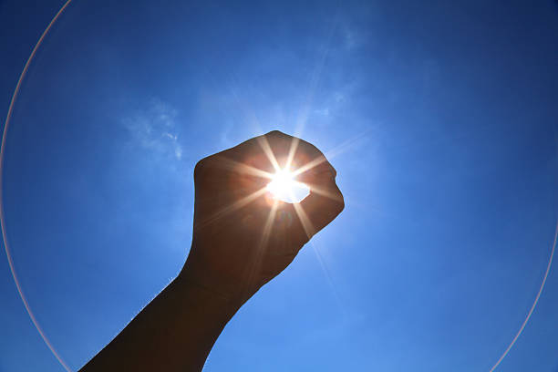 Hand raised towards sky encircling sun