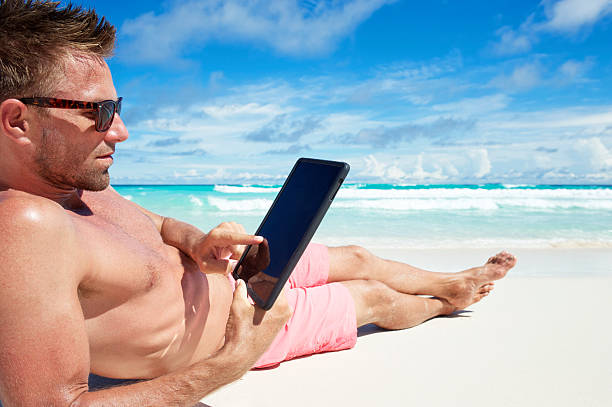 homme pose sur plage tropicale à l'aide de tablette numérique ordinateur - reading beach e reader men photos et images de collection