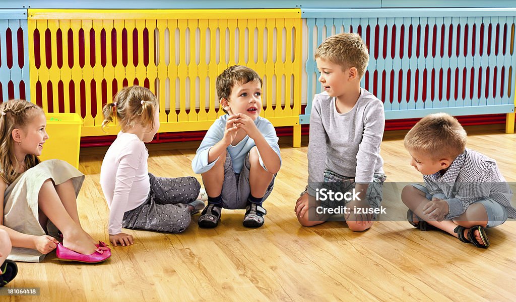 Children in Nursery School A nursery school children sitting on the floor in a playroom and talking. Child Stock Photo