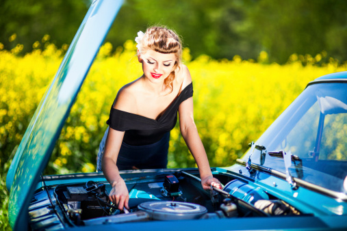 Beautiful young woman trying to repair her car in rural scenery.