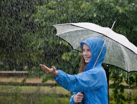 Preteen girl reaching out to touch the rain while holding an umbrella during a rainfall in the backyard
