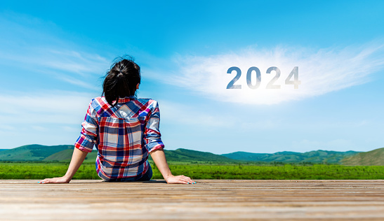 Woman sitting on wooden sidewalk, with 2024 year written on white clouds