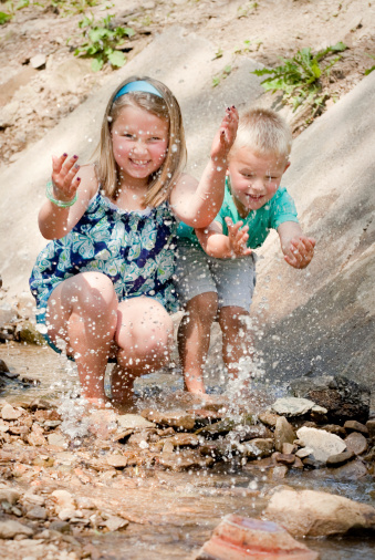 A beautiful 7 year old girl and her cute 5 year old brother splashing in a creek and laughing.