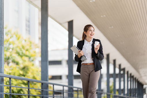 Smiling businesswoman with tablet and coffee cup going to work early in morning.