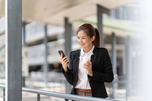 young asian business woman wearing suit using application on cell phone, read news on smartphone, fast connection, checking mobile apps outdoors - news of the world imagens e fotografias de stock