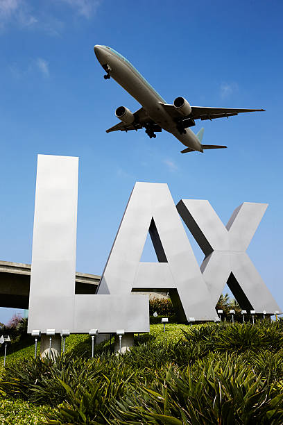 Sign Airplane flying over LAX sign in Los Angeles, California.  Clear blue sky in background.  Green grass around in front of LAX sign and bridge in background. lypsela2013 stock pictures, royalty-free photos & images