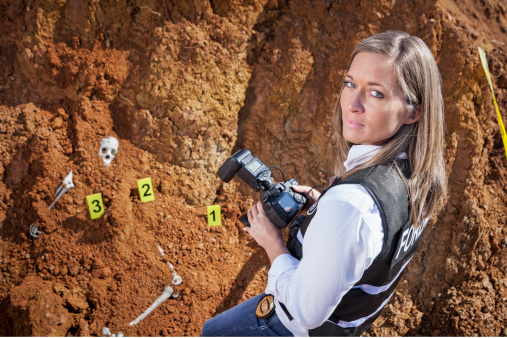 Female crime scene investigator photographing evidence at the scene of an uncovered skeleton.