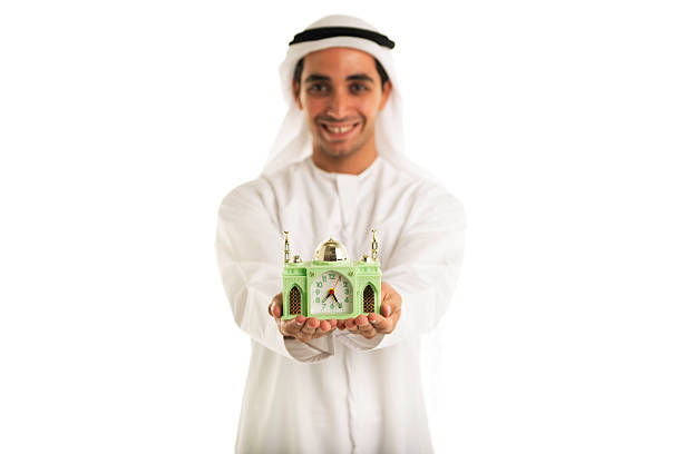 Local Emirati (from the United Arab Emirates) man, holding a small mosque, displaying the time for breaking the fast.