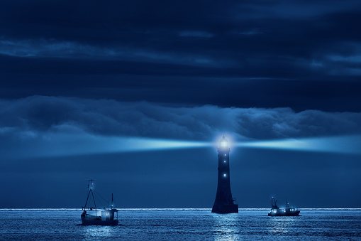 Lighthouse and ships in the night. Original shot was taken in Northern Ireland, at the Haulbowline lighthouse. Haulbowline is a main sea light and also serves to guide vessels from seaward through the entrance channel into Carlingford Lough. It is built on a wave-washed rock, exposed only at low tide. It is located in the middle of the entrance to Carlingford Lough, just on the northern side of the border between Ireland and Northern Ireland. Accessible only by boat.