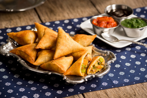A plate of samosas - a vegetarian dish commonly found in Indian restaurants - with onion-tomato chutney, mint-coriander chutney and tamarind sauce for dipping.