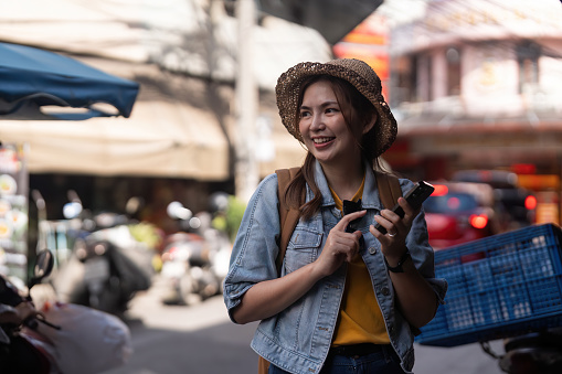 Happy young Asian tourist woman using smartphone on street with market background, Female traveller in Chiang mai enjoy shopping market during holidays.
