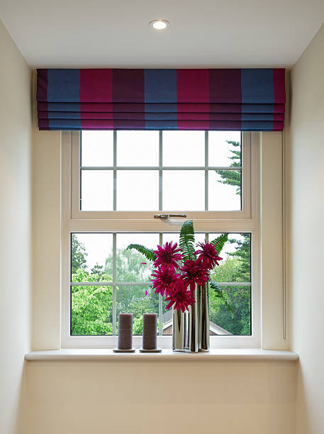 bright window with blinds and red flowers a Geogian style sash window with colourful blinds overhead and complementary red flowers in a modern chrome vase below, next to two brown candles. In the background is a bright view to a garden with lots of trees. window latch stock pictures, royalty-free photos & images