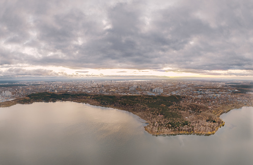 Autumn forest on lake shore at sunset and city on horizon, aerial view. Lake Shartash and Yekaterinburg, Russia
