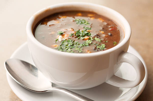 A large cup of black bean and vegetable soup topped with sour cream and cilantro.More soup: