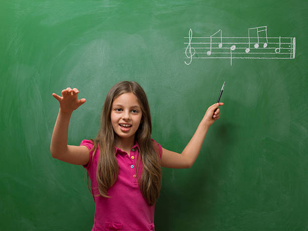Little girl directing chorus for music before blackboard Little girl directing choir for music before blackboard conductors baton photos stock pictures, royalty-free photos & images