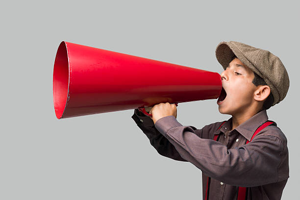 istock Little boy with newsboy cap shouting on old fashioned megaphone 181074501