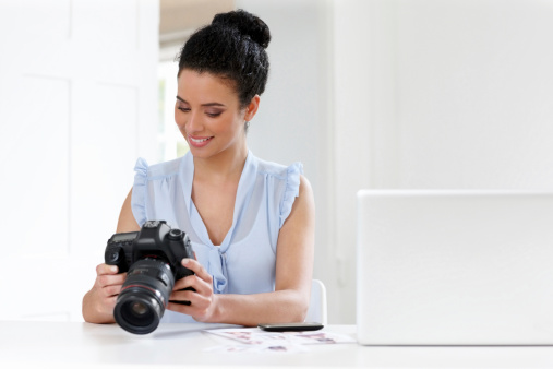 Smiling young female photographer checking pictures in camera at her desk