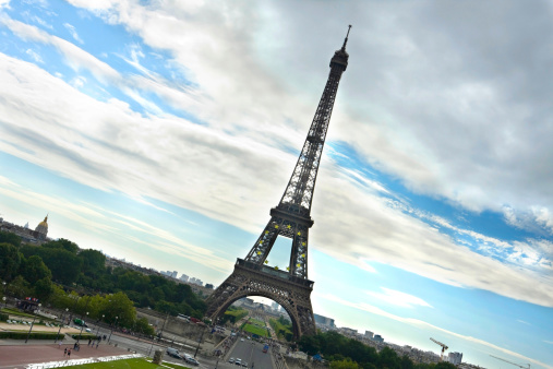 Tourists and a distinctive green car frame a wide-angle shot of the iconic Eiffel Tower in Paris, France