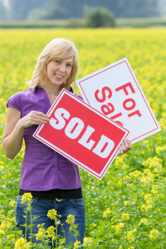 Portrait of mid adult woman holding For Sale and Sold sign in field. Vertical shot.