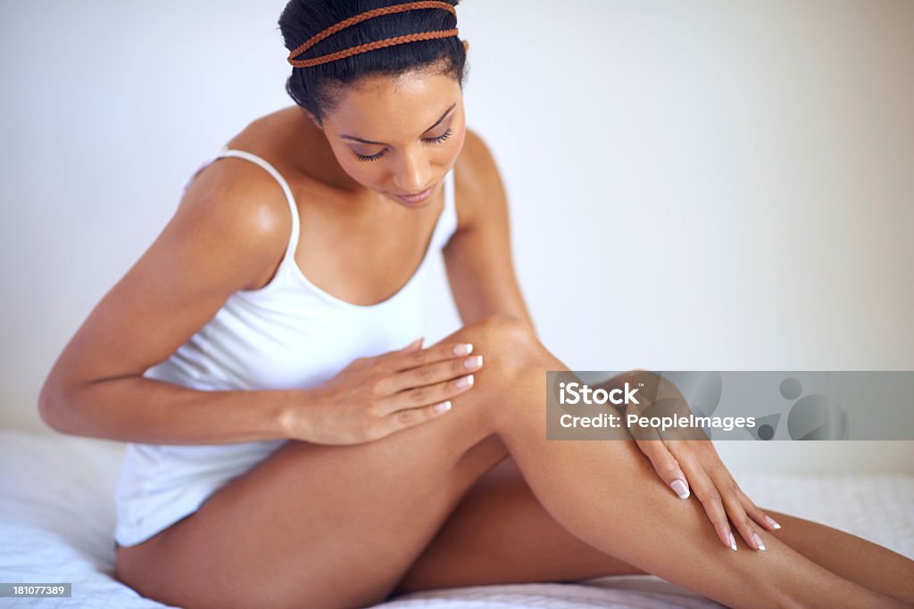 She takes skincare seriously A gorgeous young woman caressing and looking at her leg while sitting on her bed Women Stock Photo