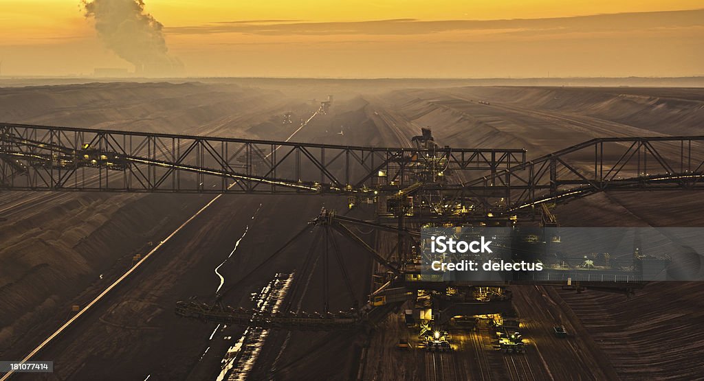 Brown coal opencast mining and monster machine Evening fog in a brown coal mining. Photo shows the largest overburden conveyor bridge F60 and a coal excavator. On the horizon, the sun sets in the mist and lignite power plant. Panorama created from 5 frames. Mining Jänschwalde, Brandenburg, Germany. Conveyor Belt Stock Photo
