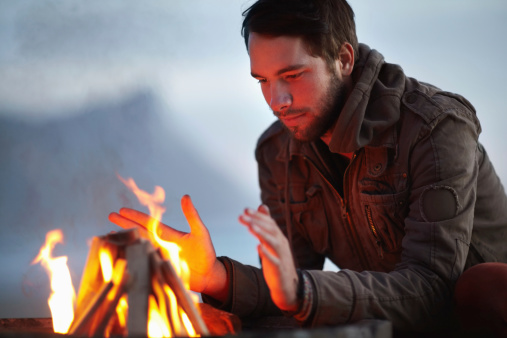 Handsome young man sitting by an open fire