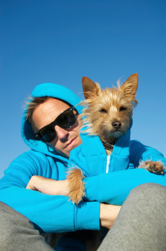 Man sits with dog each in matching blue hooded sweatshirts bright blue sky