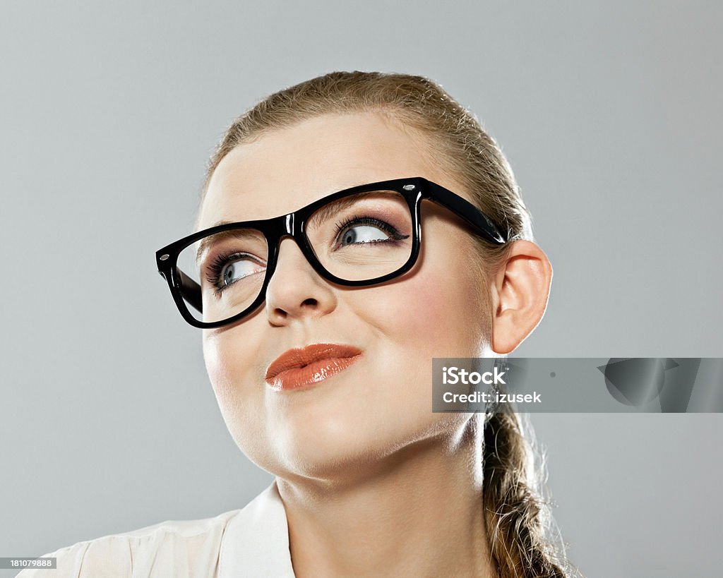 Day dreaming Portrait of  young adult woman wearing nred glasses, looking up and day dreaming. Studio shot on grey background. 20-24 Years Stock Photo