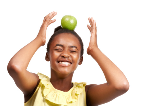 Studio shot of a young african american girl balancing an apple on her head isolated on white