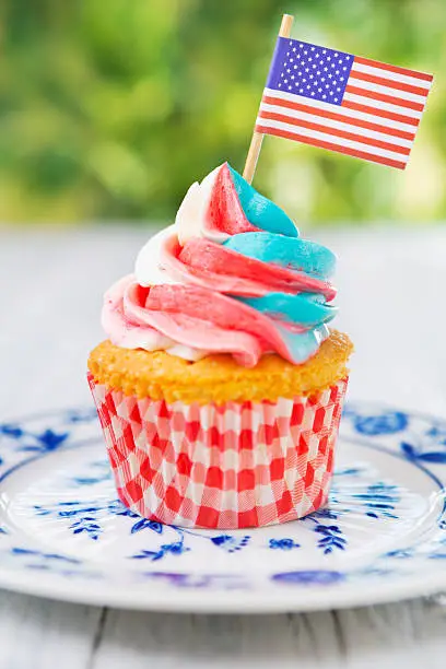 Red-white-and-blue cupcake with an American flag on an outdoor table.