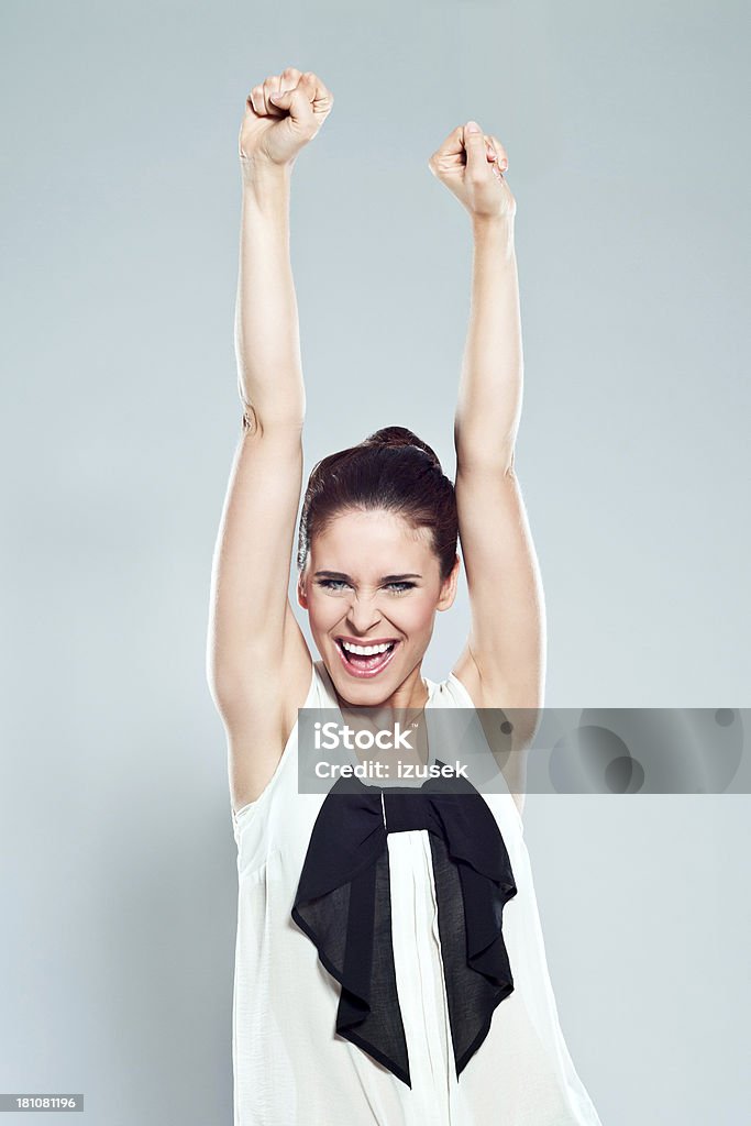 Success Portrait of attractive young woman raising her fists and laughing at the camera. Studio shot. 20-24 Years Stock Photo