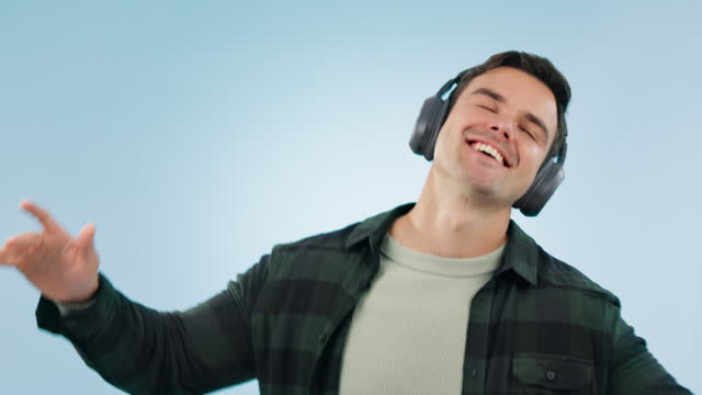 Happy, dance and man with music headphones in studio for freedom, energy or celebration on blue background. Moving, face and male model with radio earphones or streaming subscription to audio podcast