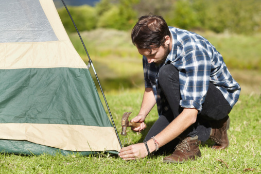 Handsome young man hammering a tent peg into the ground