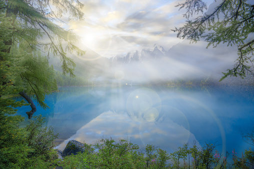 Misty morning on a mountain lake. The lake is deep blue. In the background are snowy mountains. Magic landscape with fog. Mountains are reflected in the water