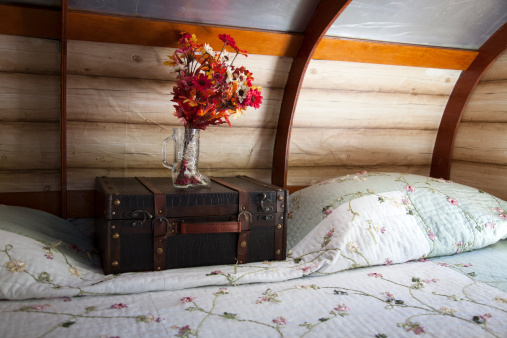 A storage chest sits on the bed inside of a vintage camping trailer.
