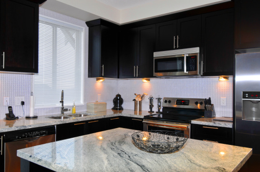 A kitchen detail with white cabinets, a brown metal range hood, white marble countertops and backsplash, and gold pendant lights.