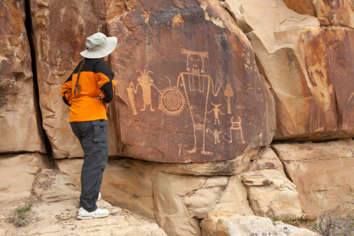 A woman looks at the famous and beautiful McKee Spring petroglyphs which stand on a cliff face in Utah's northern part of Dinosaur National Monument. Carved by the Fremont people about 1000 A.D., the scene show mysterious figures, one which looks to carrying a spiraled shield.