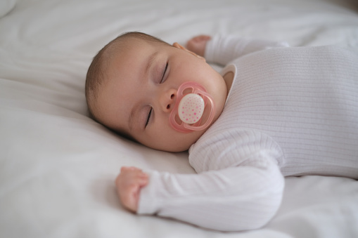 Close-up shot of Baby Girl Sleeping Peacefully With Pacifier on Her Mouth. Concept : Baby Lying on Bed