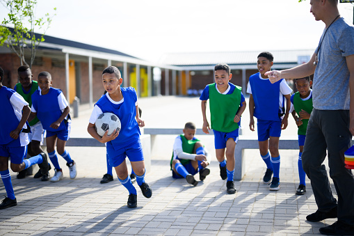 Four cute intercultural kids in activewear sitting on green grass of football field and making pile of hands while expressing their friendship