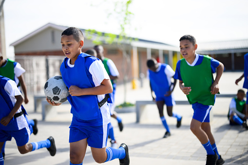 Schoolboys getting ready for soccer practice. Pulling on sock and shoes and greeting coach. School in rural area.