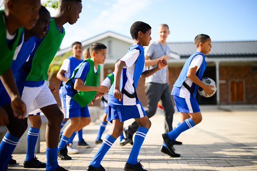 Schoolboys getting ready for soccer practice. Pulling on sock and shoes and greeting coach. School in rural area.