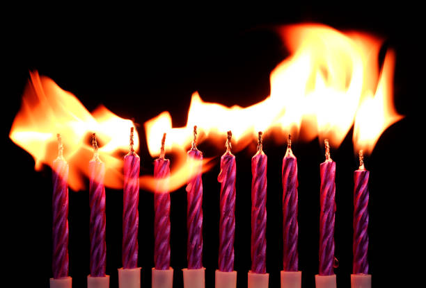 Ten purple birthday candles burning on black background.