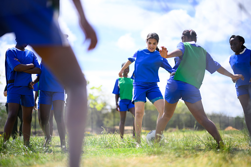 Schoolgirls playing soccer in teams on grass outside rural school