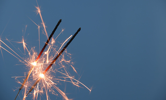 Two Christmas sparklers burning on blue background, copy space for text.