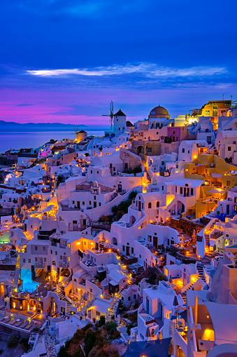 Beautiful view of Oia village with traditional whitewashed houses and windmills, Santorini island, at sunset, Greece. Scenic travel background, famous destination, colorful sky and clouds.