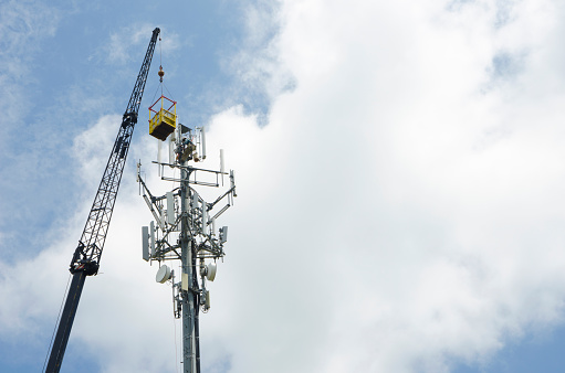 A Cellular/Television/Radio/Communications Tower is being constructed with the aid of a large crane.