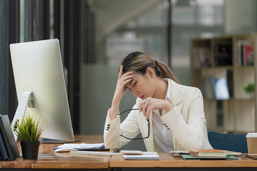 An Asian businesswoman working on a desktop computer is stressed has a headache, and thinks hard from work at the office.